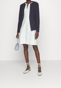 Blazer bleu marine, robe vert clair, ballerines vert menthe avec liens à la cheville, petit sac à main bleu clair. Tissu lisse et coupe ajustée.