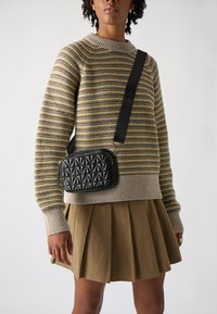 Pulover tricotat cu dungi în tonuri de bej și muștar, asociat cu o fustă plisată kaki. O geantă crossbody neagră, matlasată, adaugă contrast.