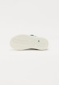 Světlomodrá teniska s texturovanou svrchní částí, bílou gumovou podrážkou s vlnitým vzorem a zeleným detailem poblíž paty.