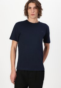 Camiseta de manga corta de color azul marino, hecha de una tela suave y lisa, con un cuello redondo y un discreto detalle de logo en el pecho.