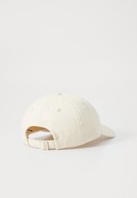 Cappellino da baseball in cotone crema con fascia regolabile, visiera curvata e dettagli di cucitura sulla parte superiore e posteriore. Apertura posteriore visibile.
