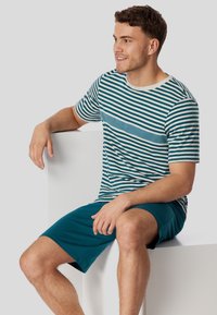 Striped t-shirt in teal and cream, with short sleeves and a round neck, paired with teal shorts. Smooth fabric, casual fit.