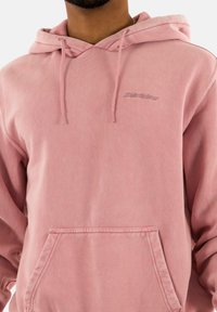 Sudadera con capucha rosa hecha de tela suave, con un bolsillo frontal y un logo bordado en el lado izquierdo del pecho. Ajuste cómodo con capucha ajustable.