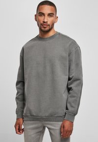 Felpa grigia a girocollo con colletto e polsini a costine, caratterizzata da una texture liscia e una vestibilità rilassata. Indossata con jeans grigi chiari.