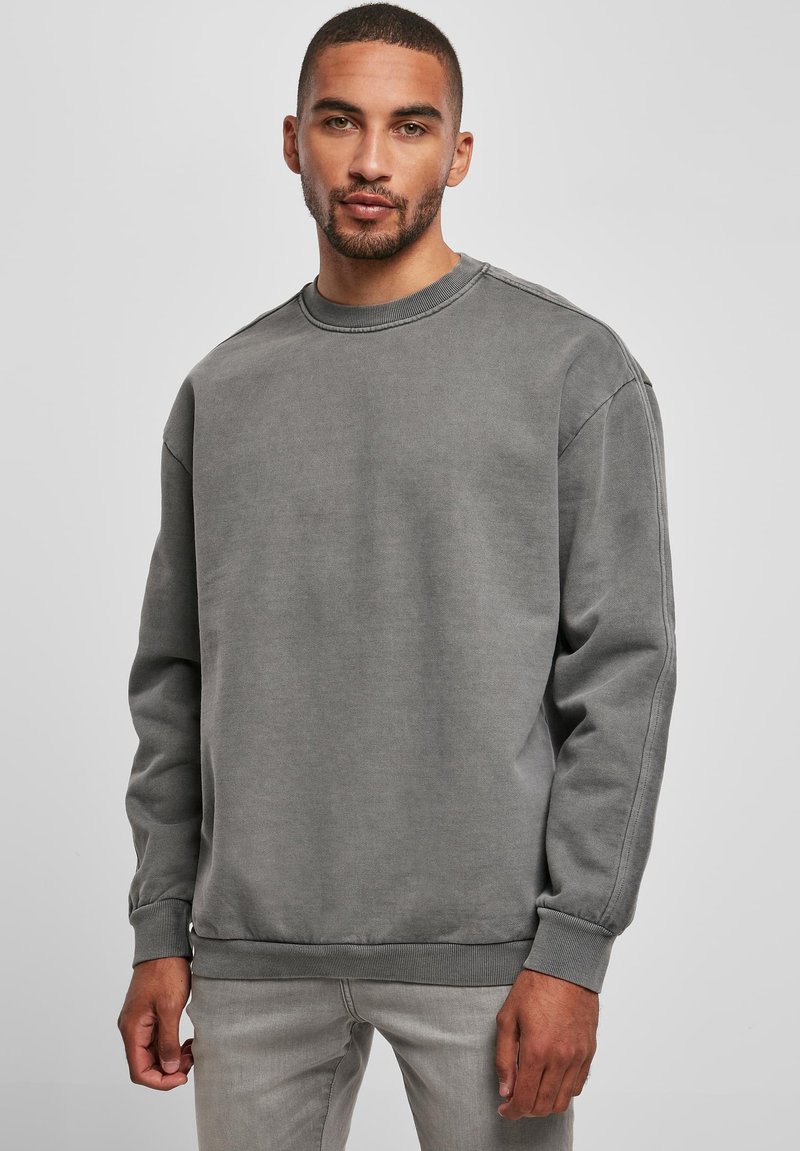 Felpa grigia a girocollo con colletto e polsini a costine, caratterizzata da una texture liscia e una vestibilità rilassata. Indossata con jeans grigi chiari.