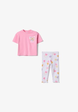 Camiseta rosa de manga corta para niño pequeño con dibujo de ratón de dibujos animados y corazones, combinada con leggings blancos acanalados con patrones de corazones multicolores.
