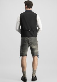 Schwarze ärmellose Weste über einem weißen Hemd, kombiniert mit strukturierten grauen Shorts. Merkmale sind ein Gurt-Detail auf der Rückseite und blaue Akzente.