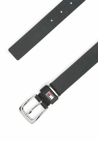 Cinturón de cuero negro con una hebilla de metal plateado, que presenta un parche decorativo con logo y múltiples orificios de ajuste a lo largo de su longitud.