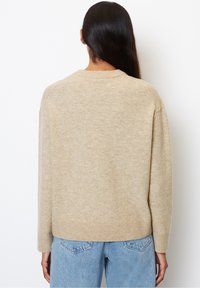 Pull en maille beige avec un col rond, des poignets et un ourlet côtelés, une coupe ample et une texture douce, associé à un jean bleu clair.
