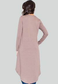 Tunique mauve à manches longues avec un ourlet arrondi et une texture douce, portée avec un jean foncé. Pas d'ornements ou de motifs visibles.