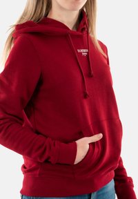 Sudadera de algodón roja con un bolsillo delantero, capucha con cuerda de ajuste y logotipo bordado en el pecho. Puños y dobladillo acanalados; textura suave.