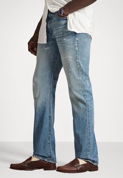 Jasnoniebieskie dżinsy o prostym kroju, z przetarciami, plamami farby i lekko postrzępionym dołem. W połączeniu z brązowymi mokasynami.