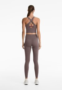 Lila idrottstopp med korsade band och skärning i ryggen, i kombination med matchande högmidjade leggings, båda i en mjuk textur.