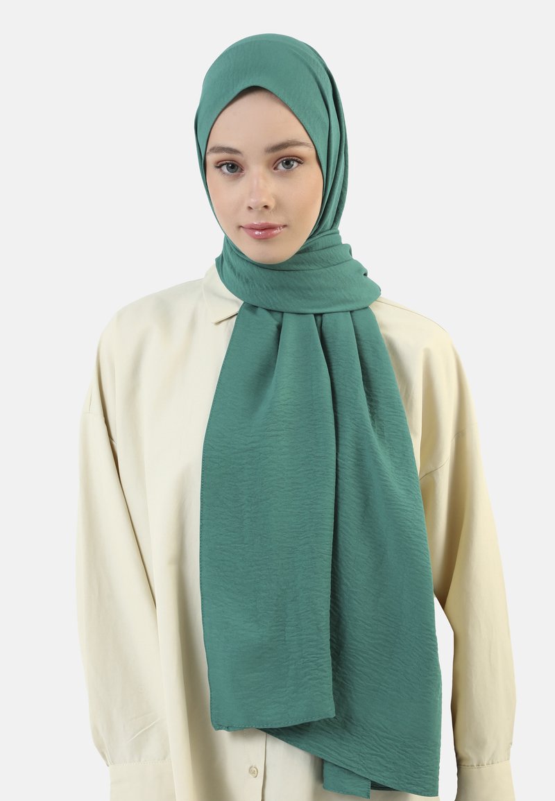 Sciarpa turchese realizzata in un tessuto leggero e texture, drappeggiata in modo elegante, indossata con una blusa color crema. Morbidi panneggi e finitura liscia.