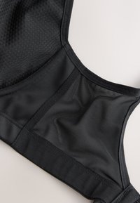 Close-up van een zwarte sportbeha met meshstofpanelen en solide stiksel details op een lichte achtergrond.