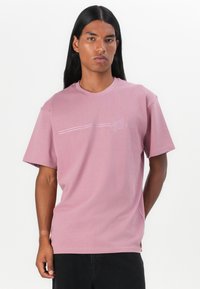 Lichtroze t-shirt met korte mouwen van katoen. Heeft een subtiele horizontale lijn en een rond logo op de linkerkant van de borst. Standaard pasvorm.