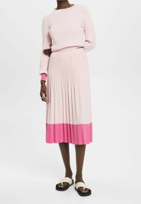 Pull en maille côtelée rose clair avec un col rond et des manches longues, associé à une jupe plissée affichant un dégradé du rose clair au rose vif.