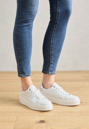 Baskets blanches en cuir avec une surface texturée, bout rond et une semelle épaisse. Des lacets et des œillets en métal sont présents pour le maintien.