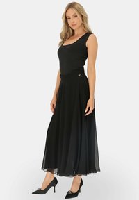 Czarny top bez rękawów zestawiony z lekką, zwiewną czarną spódnicą o dopasowanej talii i subtelnej połysku, uzupełniony czarnymi szpilkami.