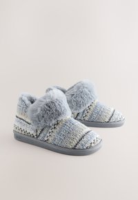 Chaussons tricotés bleu et jaune à motifs avec garniture en fausse fourrure grise et semelles en caoutchouc grises. Texture douce avec un design confortable.