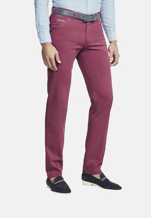 Man draagt slim-fit bordeauxrode broek, zwarte riem, lichtblauw overhemd met lange mouwen en zwarte loafers met witte zolen en decoratieve stiksels.