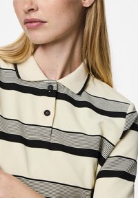 Crème polo shirt met zwarte horizontale strepen, voorzien van een kraag en een knoopsluiting met drie knopen. Gladde stof met een ribbelstructuur.