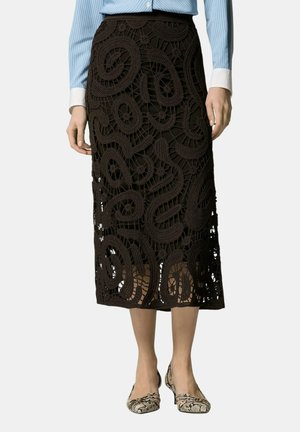 Gonna midi nera all'uncinetto con motivo traforato a vortice, indossata con camicia a righe blu e décolleté basse con stampa serpentata.