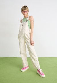 Stripete, lyse overaller med justerbare stropper, sammen med en grønn ribbestrikket tanktop og rosa platåsneakers. Glatt bomullstekstur.