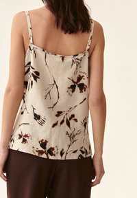 Mouwloze top met bloemmotief in lichtbeige stof, voorzien van donkerbruine botanische prints. De achterkant heeft dunne banden voor ondersteuning.