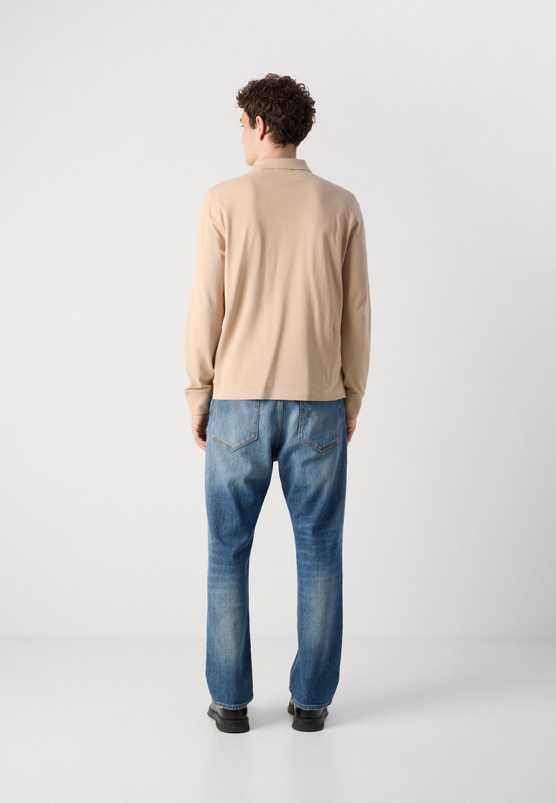 Beige Langarmhemd mit weichem Stoff und Kragen, kombiniert mit hellblauen Denim-Jeans mit Gesäßtaschen, getragen mit schwarzen Schuhen.