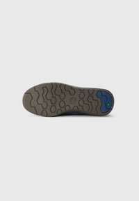 Sola do sapato com padrão de ranhura hexagonal e zig-zag, logo da Timberland no centro, e uma seção azul com hexágono verde perto do calcanhar.