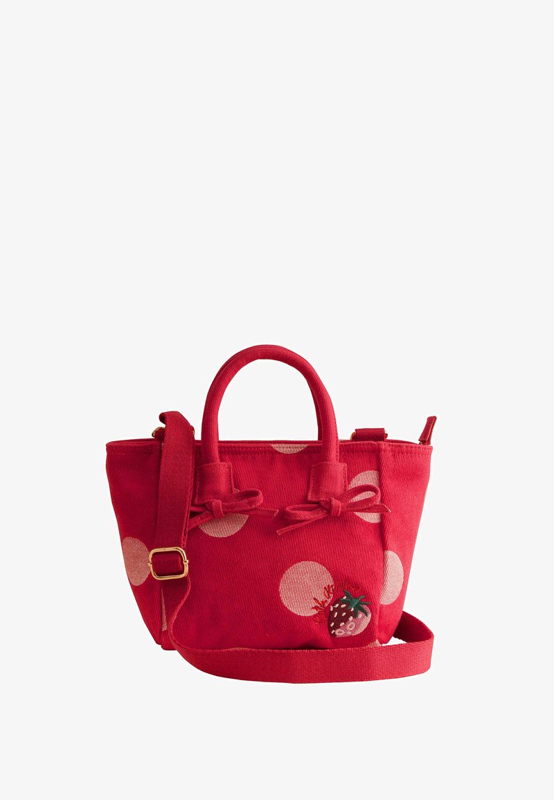 Petit sac à main en tissu rouge avec des pois blancs, des nœuds à l'avant, une bandoulière réglable et une broderie de fraise dans un coin avant.