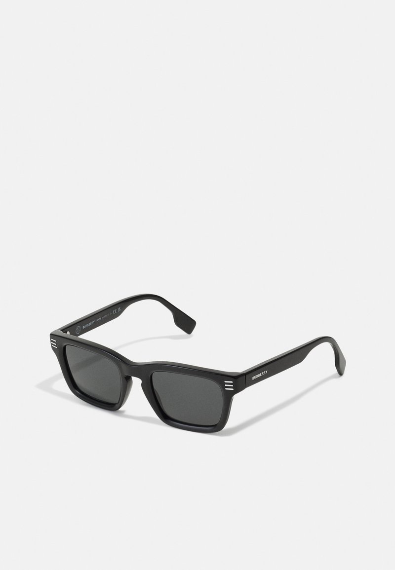 Black sunglasses with a rectangular frame, matte finish, dark lenses, and three horizontal stripes on each temple. Minimalist design.