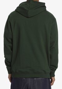 Felpa verde con una texture morbida, dotata di un grande cappuccio, polsini e orlo a coste. Design posteriore senza cuciture, senza motivi o loghi visibili.