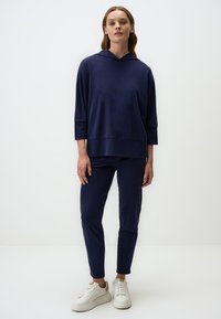 Set di abbigliamento da lounge blu navy composto da una maglia con cappuccio e maniche a tre quarti e pantaloni aderenti, realizzato in tessuto morbido e liscio. Include sneakers bianche.