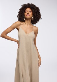 Abito in lino beige con scollo a V, spalline sottili e silhouette fluida. Il tessuto testurizzato aggiunge profondità; presenta tasche laterali per praticità.