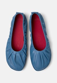 Pár modrých kožených baletních plochých bot s nařasenými elastickými okraji a červenými vnitřními stélkami, pohled zeshora na bílém pozadí.
