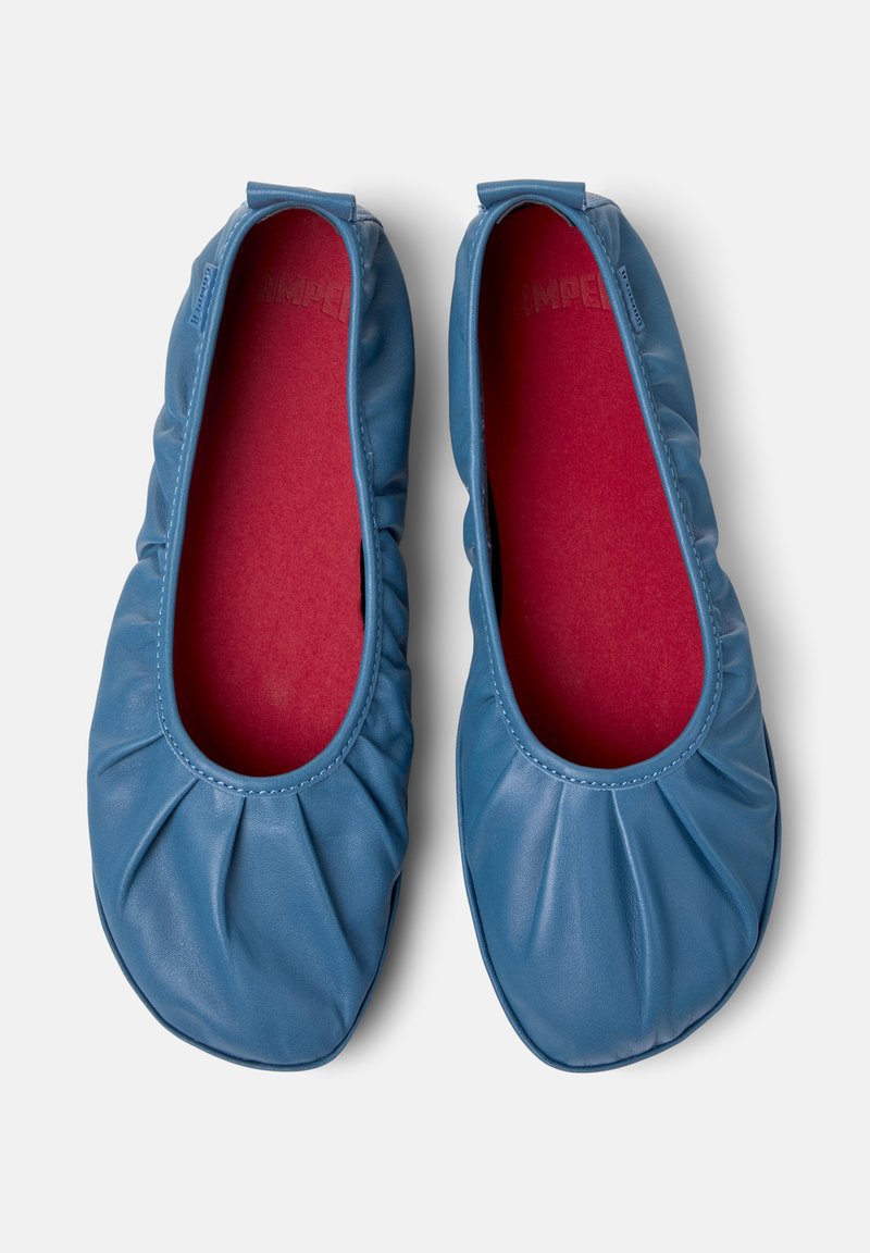 Ett par blå läder ballerina skor med samlade elastiska kanter och röda innersulor, sedda uppifrån mot en vit bakgrund.