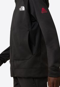 Fekete cipzáras dzseki puha, sima anyagból. Magas gallérral, két oldalzsebbel, valamint fehér és piros logókkal a mellkason és az ujján.