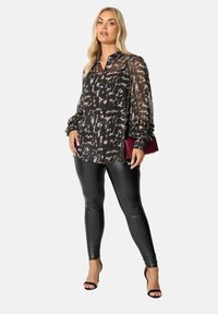 Blusa nera trasparente con stampa animale, maniche a volant e chiusura con bottoni, abbinata a leggings neri lucidi e tacchi a strappo neri.