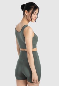 Sujetador deportivo verde oscuro y pantalones cortos de talle alto a juego, hechos de un material suave y elástico, con un diseño sin costuras y sin hardware visible.