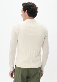 Kötött pulóver off-white színben, texturált bordás mintázattal, hosszú ujjal és kerek nyakkal. Az ujjak vége és az alsó szegély bordás.