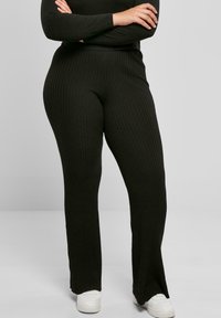 Mørkegrønne ribbestrikkede bukser med bred bunndesign, som har høy midje og en teksturert overflate. Stylet med hvite joggesko.