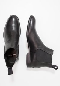 Bottes Chelsea en cuir noir avec panneaux latéraux élastiques, bout arrondi et languette à l'arrière. Texture lisse avec un talon bas.