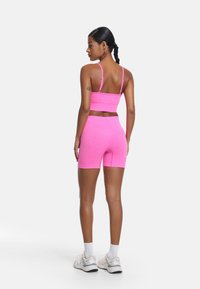 Rosa träningsset som består av en kort topp med tunna axelband och högmidjade cykelshorts, båda gjorda av ett mjukt, stretchigt tyg.