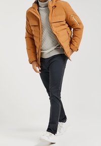 Pomarańczowa, ocieplana kurtka z kapturem, szary sweter dzianinowy i granatowe spodnie. Białe trampki dopełniają strój, kurtka posiada kieszeń na zamek.