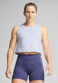 Gaiši violets sporta topiņš ar īsiem galiem un tumši zilas augsta vidukļa šorti, izgatavoti no elastīga auduma, ar logotipa detaļu priekšpusē.