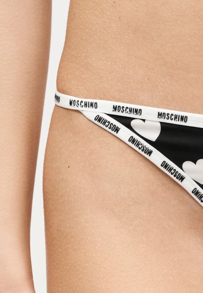 Μαύρο κάτω μέρος μπικίνι με λευκές καρδιές και λευκές ελαστικές τιράντες με την επιγραφή "MOSCHINO" μαύρο στη λεκάνη ενός ατόμου.