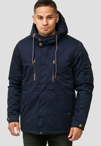Marineblå parka-jakke laget av slitesterkt stoff, med glidelåsforside, snorhette og to frontlommer med dekorative knapper.