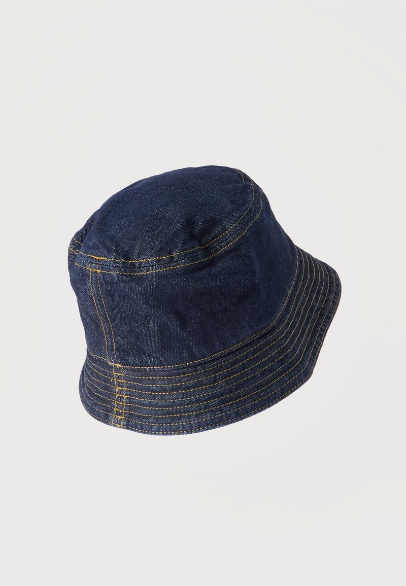 Dunkelblauer Jeans-Bucket-Hut mit sichtbaren gelben Nähten entlang der Nähte und Krempe auf hellem einfarbigem Hintergrund.